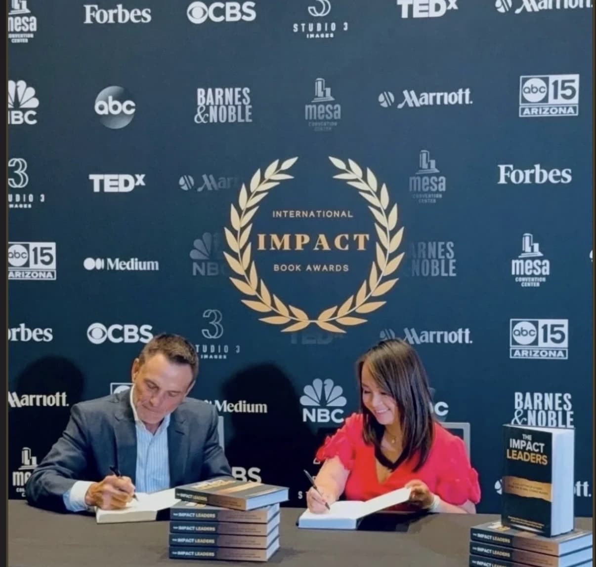 Kimly Hoang-Nakata signing copies of The Impact Leaders alongside Kevin Harrington, the original Shark from Shark Tank, at the Impact Leaders Conference in Tampa, Florida